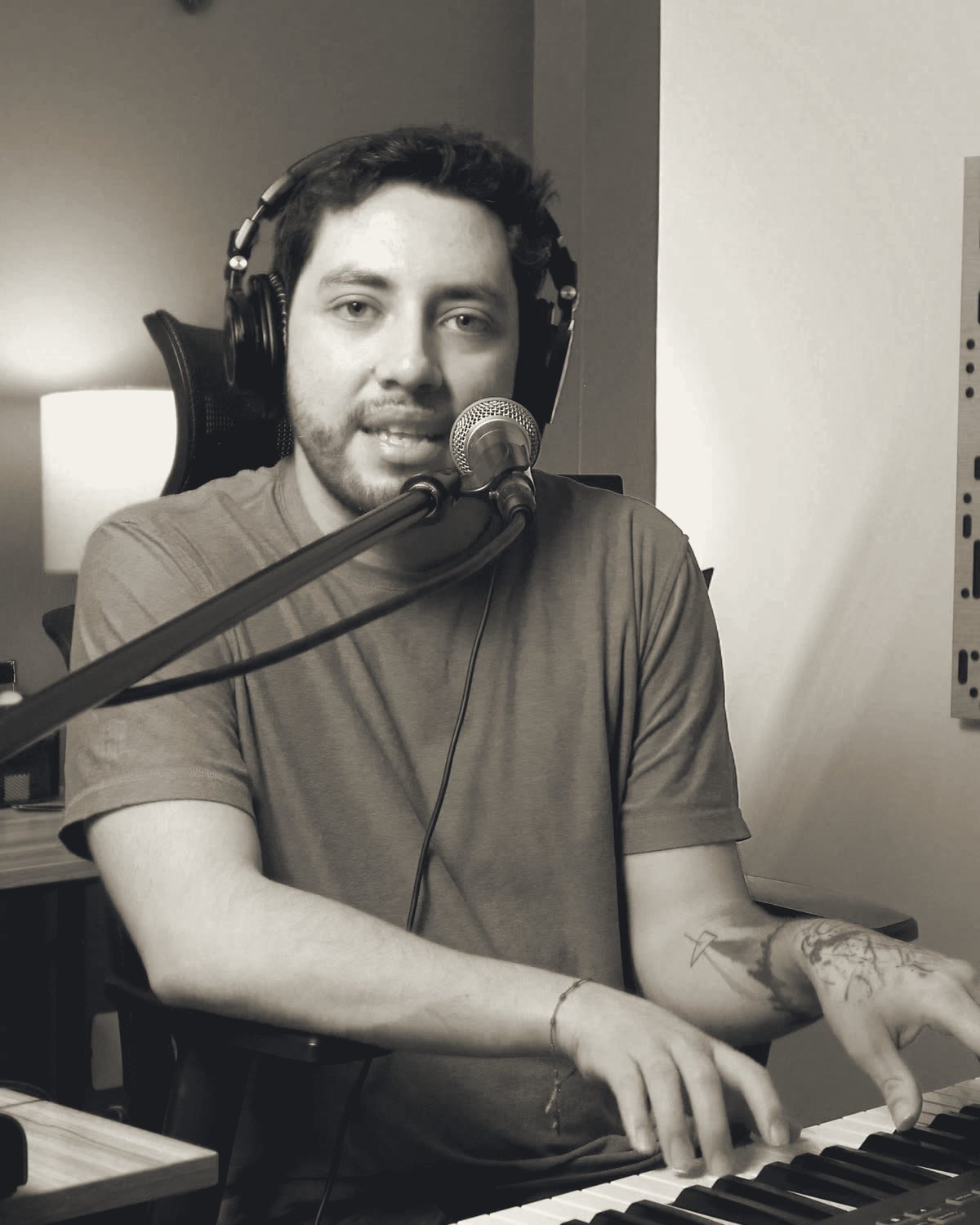Luis Aquino en su estudio, con audífonos, frente al micrófono y con las manos en el teclado